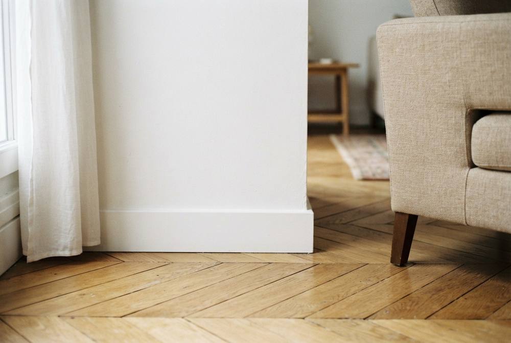 Plinthe blanche satinée au pied d'un mur blanc, posée sur un parquet en chêne en point de Hongrie